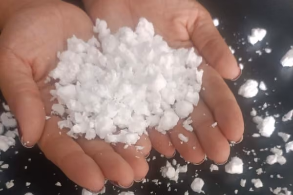 Flocos de isopor triturado nas mãos, com pedaços irregulares do material visíveis.